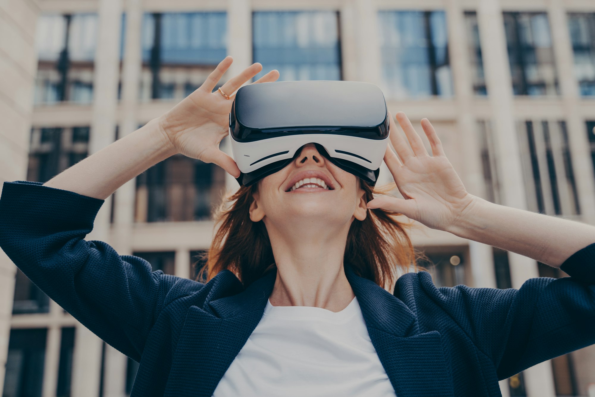 Immersed woman looking up in virtual reality while wearing portable VR, standing on city street